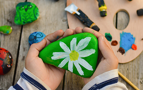 Kinderhände halten einen mit einer Blüte bemalten Stein
