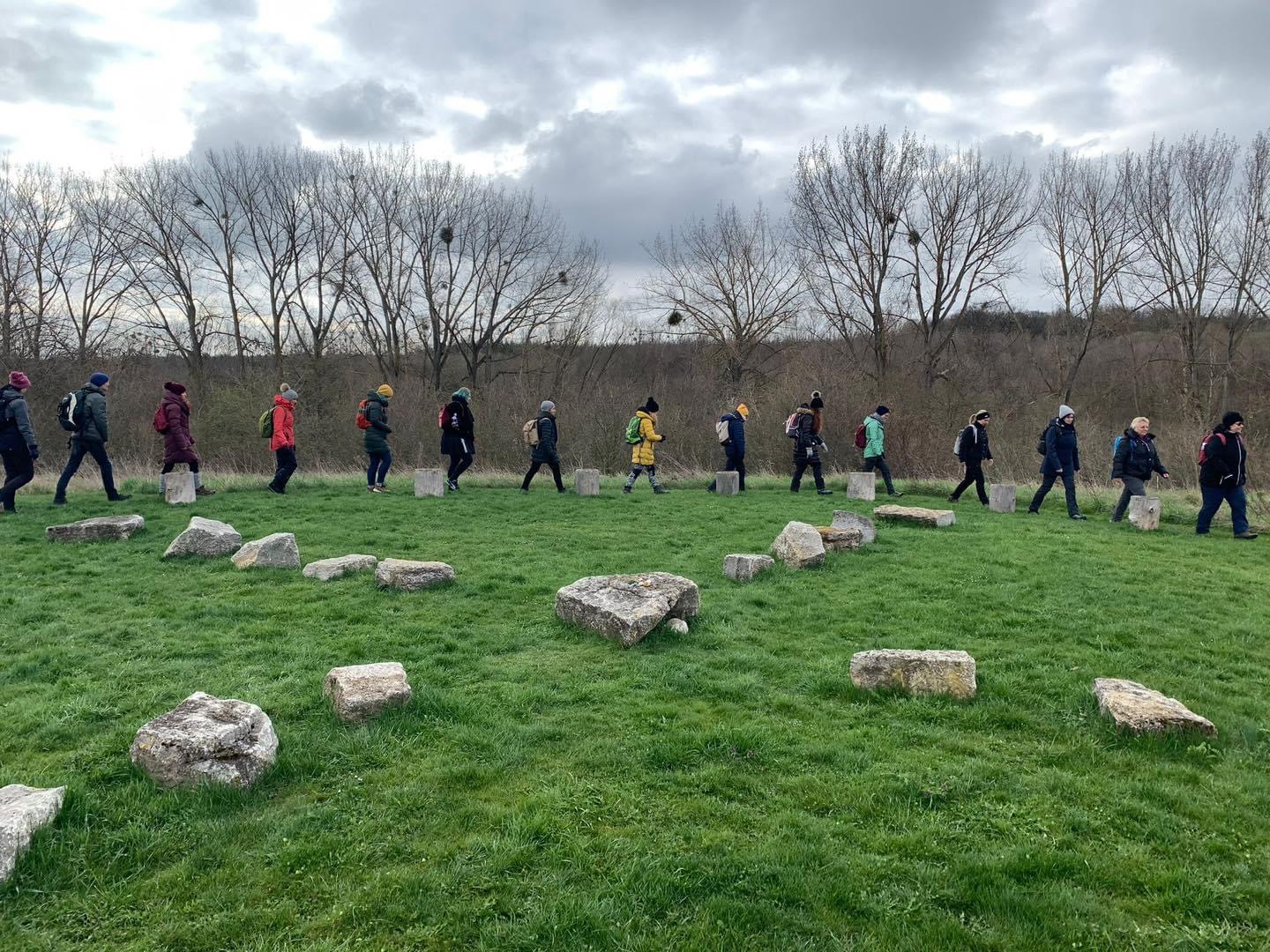Personengruppe spaziert über eine Wiese vorbei an einem Steinkreis