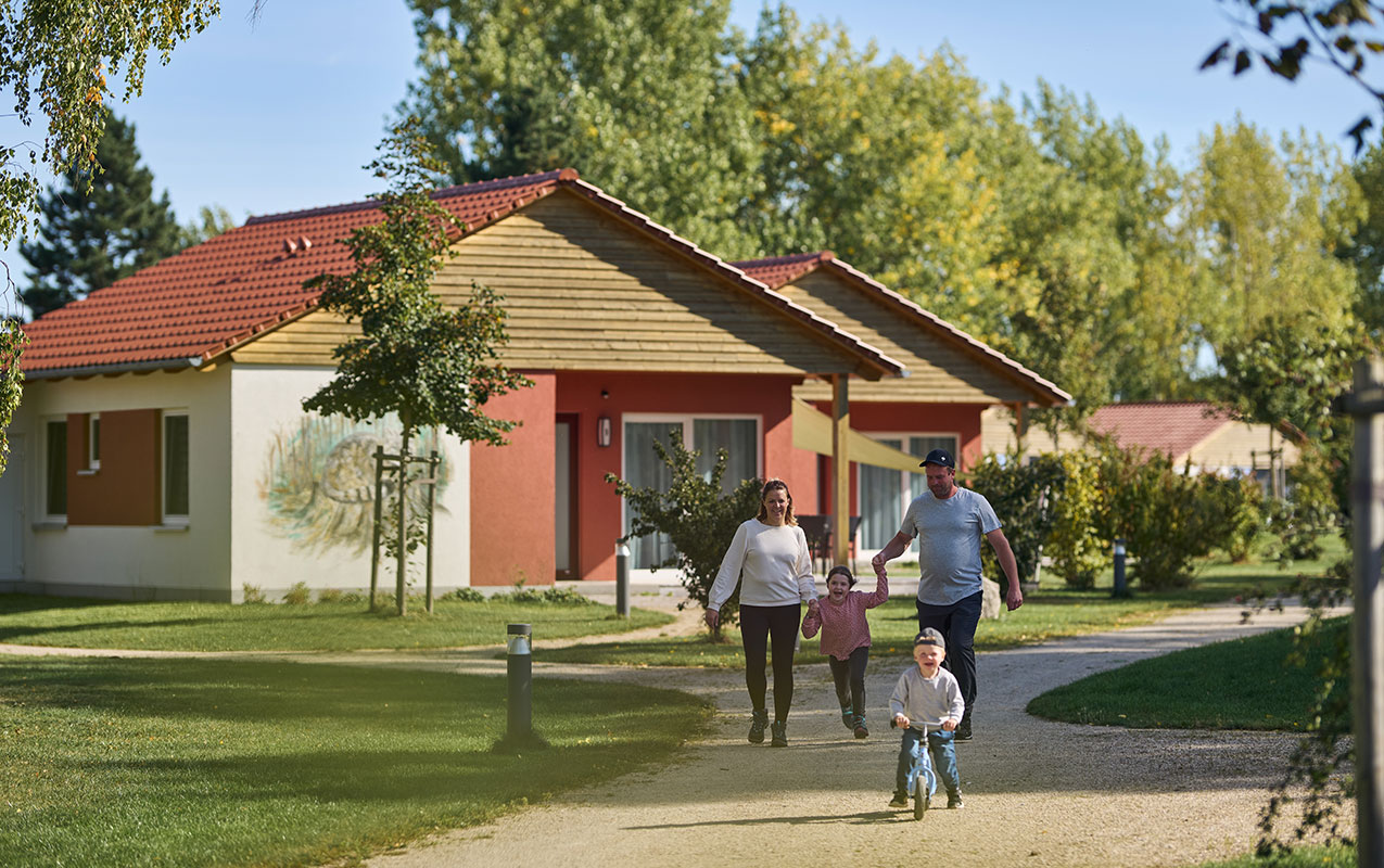 Familie mit zwei Kindern spaziert entlang der Ferienhaus-Anlage